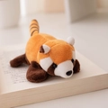 Plush red panda slap bracelet toy in orange-brown color lying on an open book - Refrigerator Magnet / Yellow
