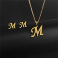Detailed close-up of golden stainless steel M-letter necklace and matching stud earrings - Letter M / Gold