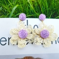 Handmade raffia flower earrings in cream white and purple woven design on a grass background - Purple Woven 3D Floral Earrings