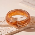 Detailed view of amber textured acrylic bangle on a beige stone surface - Light Coffee
