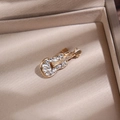 Detalle de un broche de violín dorado con diamantes en un joyero color beige - Violín / Oro-Circón Blanco