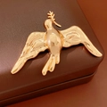 Macro shot of gold bird brooch with polished finish and olive branch on leather box - Gold