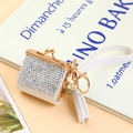 Macro detail of a white rhinestone mini bag keychain with gold clasp and tassel detail - Off-White Full Rhinestone