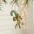 Mint green Christmas candy cane ornament with a gold sequin bow on a pine branch - Candy Cane