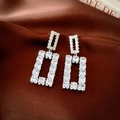 Macro shot of silver geometric square earrings with sparkling cubic zirconia on brown silk - Silver