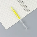 Creatieve markeerstift in spuitvorm met gele inkt op een ruitjesnotitieboek - Geel