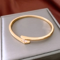 Detalle macro de un brazalete bypass dorado con incrustación de circón sobre terciopelo - Oro (Chapado En Oro Real)