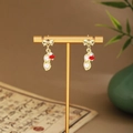 Macro shot of pearl peanut earrings with red bead details on a golden jewelry stand - Bow Peanut Pearl (E6457)