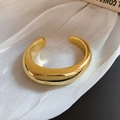 Vue détaillée d'un bracelet jonc doré poli en forme de C sur de la soie blanche texturée - Style Ovale Irrégulier Doré