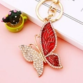 Red enamel butterfly keychain with gold finish and sparkling rhinestones on pink desk - Red Pattern Butterfly