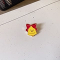 Close-up of a cartoon yellow bell brooch with a red bow on a white textured background - Bell