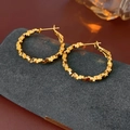 Detailed close-up of gold plated geometric hoop earrings on a dark matte pedestal - Gold