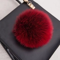 Vue macro d'un pompon en fourrure rouge duveteux avec fermoir doré sur un sac noir - Style Bouton Pression 14CM / Bordeaux