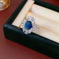 Makroaufnahme eines ovalen blauen Zirkonrings mit Halo-Effekt in einer Geschenkbox - Einstellbar Offen / Silber-Blau