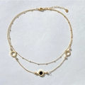 Dettaglio della collana dorata a due strati con numeri romani e ciondolo nero circolare - Oro