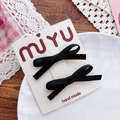 Close-up of black fabric bow hair clips on display card with rustic lifestyle background - Black