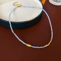 Detail einer hellblauen Perlenkette mit goldenem strukturiertem Anhänger auf Tablett - Gold-Blau