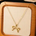 Detailed close-up of a gold-plated bow necklace displayed on a beige jewelry board - Gold Polished Bowknot Pendant Necklace