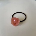 Detailed view of pink flower hair tie with a black elastic band on a white surface - Pink Jelly