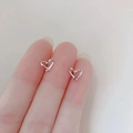 Detailed view of silver heart-shaped crisscross stud earrings held in hand - Hollow Heart / Silver