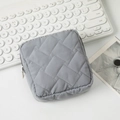 Macro shot of grey quilted fabric cosmetic bag with silver zipper on a white desk - Gray