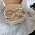 Detail view of irregular silver hoop earrings with matte texture on a beige jewelry box - Silver