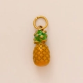 Dettaglio ravvicinato di un ciondolo a forma di ananas dorato con foglie verdi in metallo - Ciondolo Ananas
