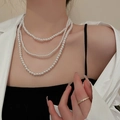 Close-up of a three-layer white pearl necklace worn with a white blazer and gold ring - White Triple Layer Style (10#) / White Pearl