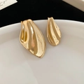 Macro view of gold asymmetrical fishtail earrings on a white ceramic tray - Gold
