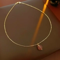 Close-up of gold-plated necklace with red-brown gemstone on dark leather surface - Necklace - Gold