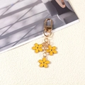 Golden keychain featuring three yellow enamel flowers on a textured beige and gray background - Yellow