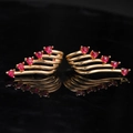 Detail of gold-plated wing earrings featuring red heart-shaped crystals on black backdrop - Red