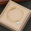 Macro shot of gold evil eye pendant on a minimalist stainless steel open bangle bracelet - Lake Blue