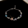 Makroaufnahme: Silbernes Kreuz-Armband mit bunten Edelsteinen auf schwarzem Samt - Silber mit bunten Steinen und Kreuz