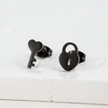 Close-up of black matte stainless steel asymmetric heart key and lock stud earrings - Heart Lock & Key / Black