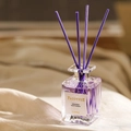 Dettaglio del flacone in vetro per aromaterapia viola con bastoncini su tessuto beige morbido - Viola