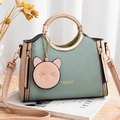 Grün-rosa Handtasche mit Ringgriff und Katzenanhänger auf einem Holztisch präsentiert - Matcha-Grün und Khaki