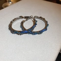 Macro shot of silver twisted hoop earrings featuring paved blue crystals and silver finish - Style 1 Silver Pin - Blue