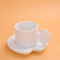White shell-shaped ceramic coffee cup and saucer set on vibrant orange background - Shell Shape Cup + Saucer - White