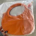 Orange saddle bag with large round handle and vertical striped texture in hand - Orange