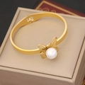 Eleganter Schmetterlingsarmreif in Gold mit Perle auf einer Champagner-Schmuckschatulle - Bangle / Gold