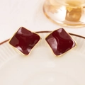Macro shot of dark red glaze square stud earrings with gold plating on a white plate - Red
