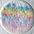 Detalle macro de cuentas de flores de resina degradada con copos dorados en plato blanco - 20g (Aprox. 110 unidades) / Degradado Mixto