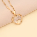 Close-up of gold heart necklace featuring a faceted crystal and filigree frame - White