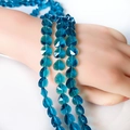 Detailed view of peacock blue faceted crystal heart beads on a hand model for DIY - Peacock Blue