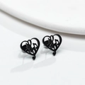 Detalle macro de pendientes de corazón con nota musical en negro mate sobre fondo blanco mínimo - Negro