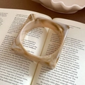 Chic beige marble-patterned acrylic thick square bangle resting on an open book - Thick Square Design / Off-white Marble