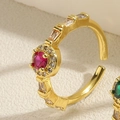 Detalle de anillo dorado abierto con piedra roja rubí redonda y circonitas laterales - Abierto Ajustable / Circonita Rojo Rosa