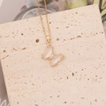 Détail du collier papillon doré avec ailes en cristal sur une surface en pierre beige - Blanc