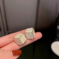 Eleganti orecchini a cubo bianchi con bordi dorati tenuti in mano primo piano - Stile Geometrico a Cubo (22# Ago d'Argento) / Bianco